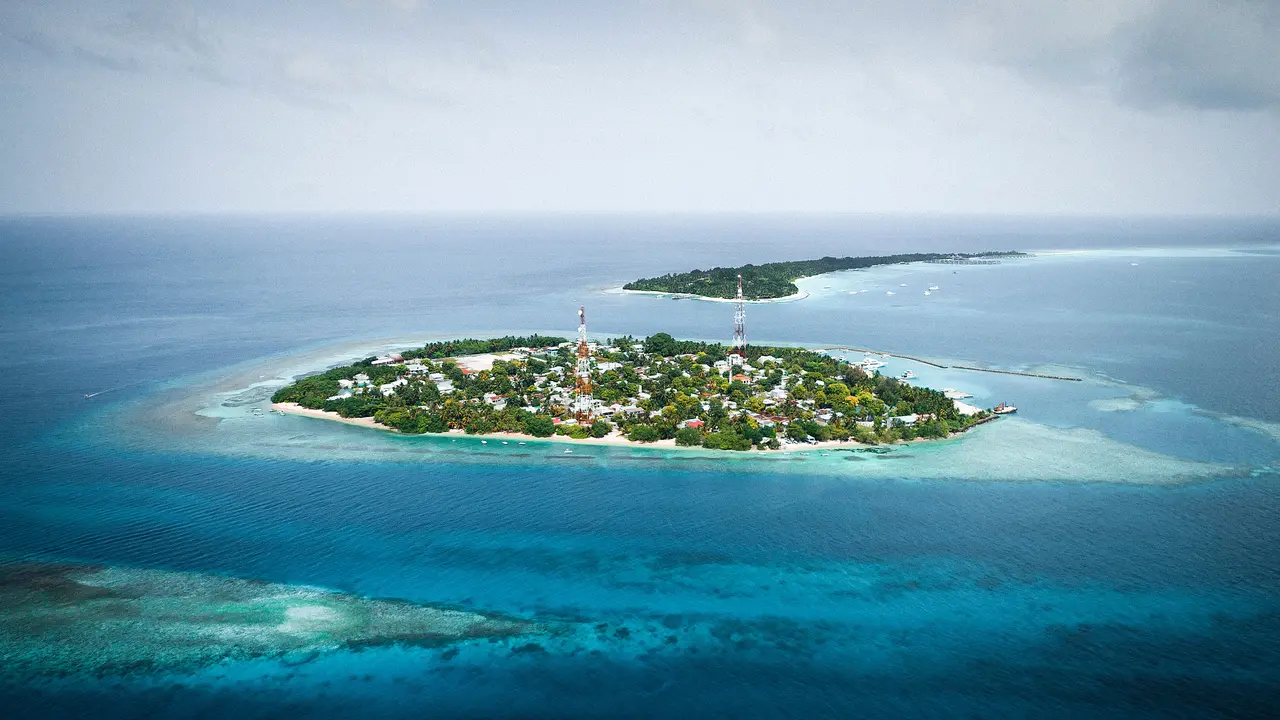 Kleine tropische Insel mit Lagune und Korallenriff im weiten blauen Meer.