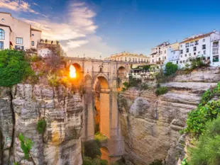 Historische Brücke über tiefer Schlucht mit Stadtblick im warmen Sonnenlicht.