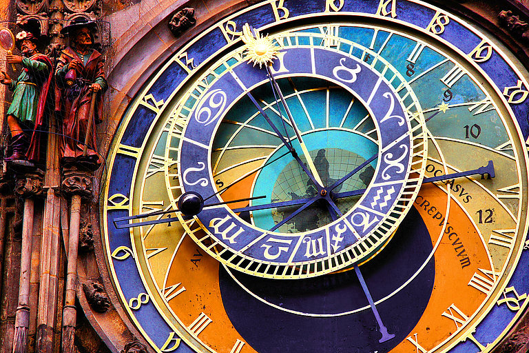 Detail einer kunstvollen astronomischen Uhr mit farbigem Zifferblatt und Zeigern.