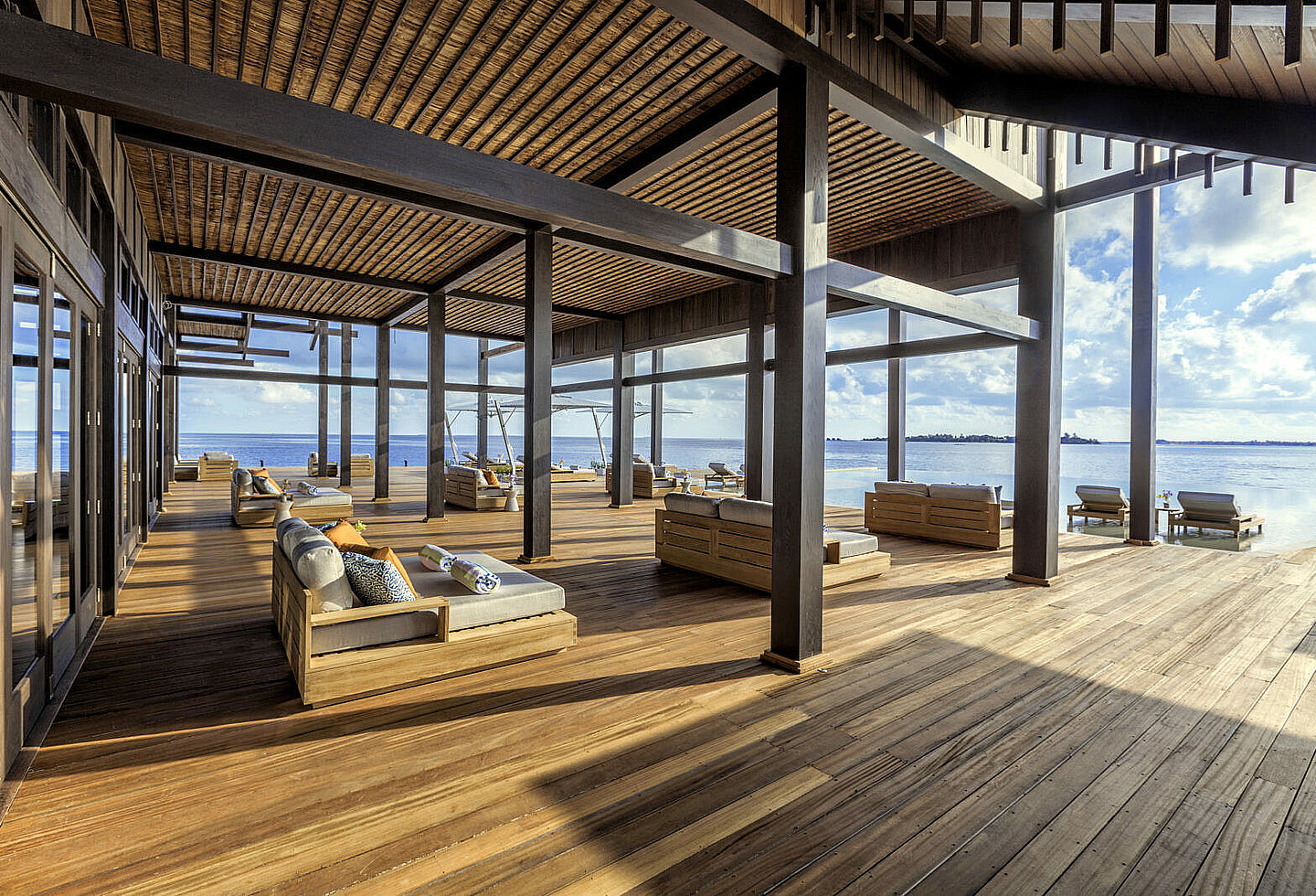 Große Holzterrasse mit Strohdach und gemütlichen Liegebetten, Blick auf Himmel und Meer