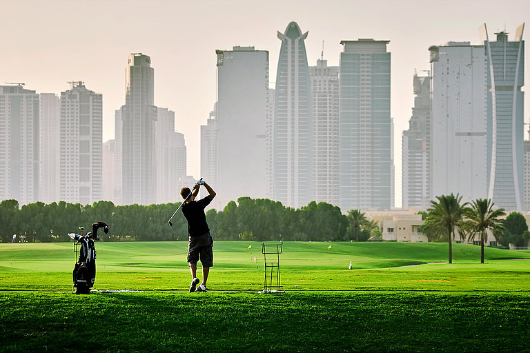 Golfer steht auf gepflegtem Golfplatz mit schöner Skyline im Hintergrund. 