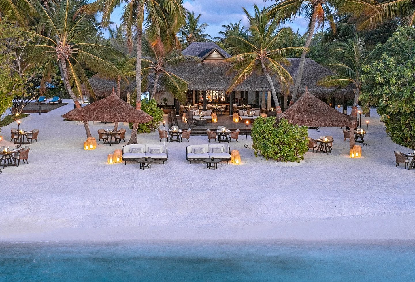 Strandabschnitt mit Liegen, Palmen und offenen Pavillons direkt am türkisblauen Meer.