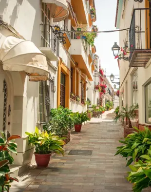 Sonnige Altstadtgasse in Marbella mit weißen Häusern, Pflanzen und Balkonen.