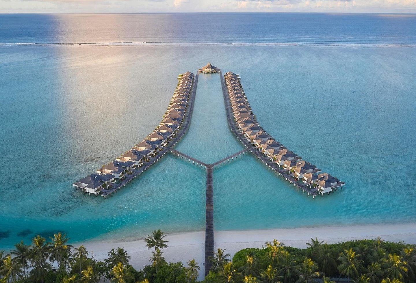 Luftaufnahme des Resorts mit Stegen, türkisfarbenem Wasser und Palmen.