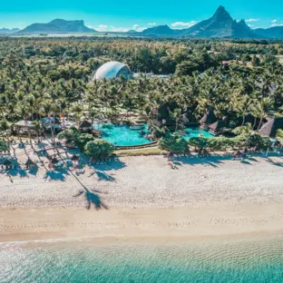 Luftaufnahme eines Palmenstrands mit Hotelanlage, türkisblauem Meer und Bergen.