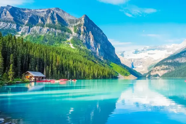 Türkisblauer Bergsee mit Bootshaus, Wald und alpiner Bergkulisse.