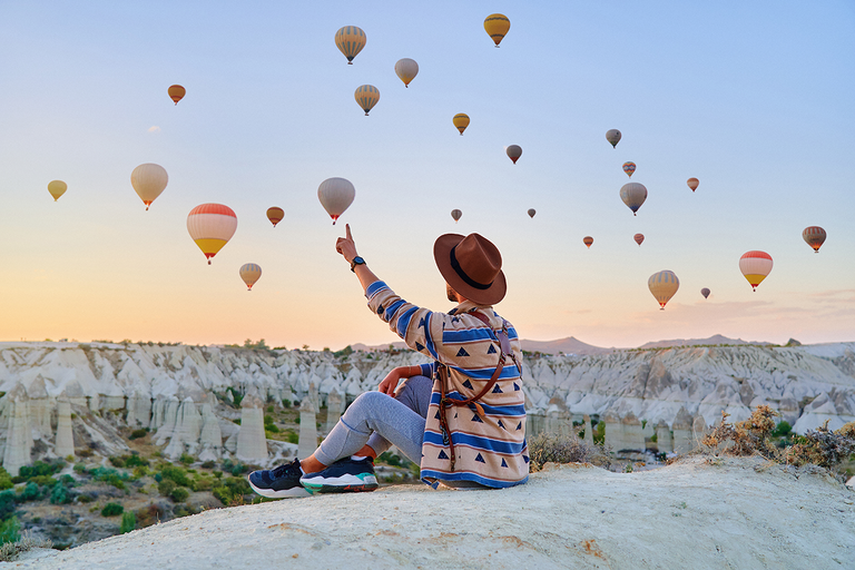 Person blickt auf Heißluftballons über weißer Felsenlandschaft in Kappadokien.