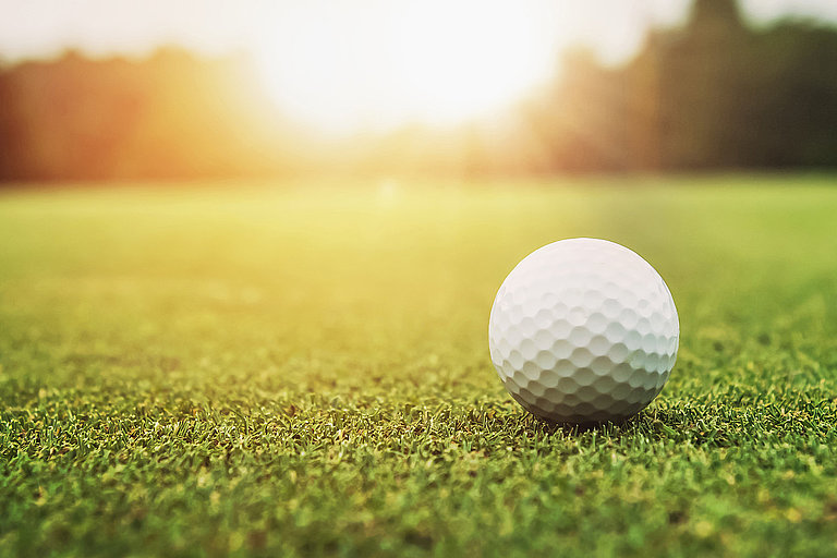Einsamer Golfball liegt auf dem Rasen, beleuchtet vom Sonnenlicht.