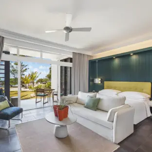 Modernes Hotelzimmer mit Sofa, Balkon, grünem Akzent und hellem Blick ins Freie.