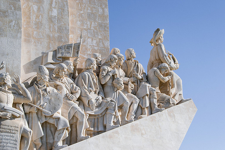 Steinerne Figuren am Denkmal der Entdeckungen in Lissabon vor blauem Himmel.