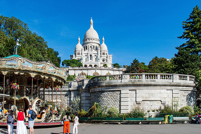 Blick auf die Basilika Sacré-Cœur und den charmanten Karussellplatz in Montmartre – ein ikonischer Pariser Moment, der an ‚Emily in Paris‘ erinnert.