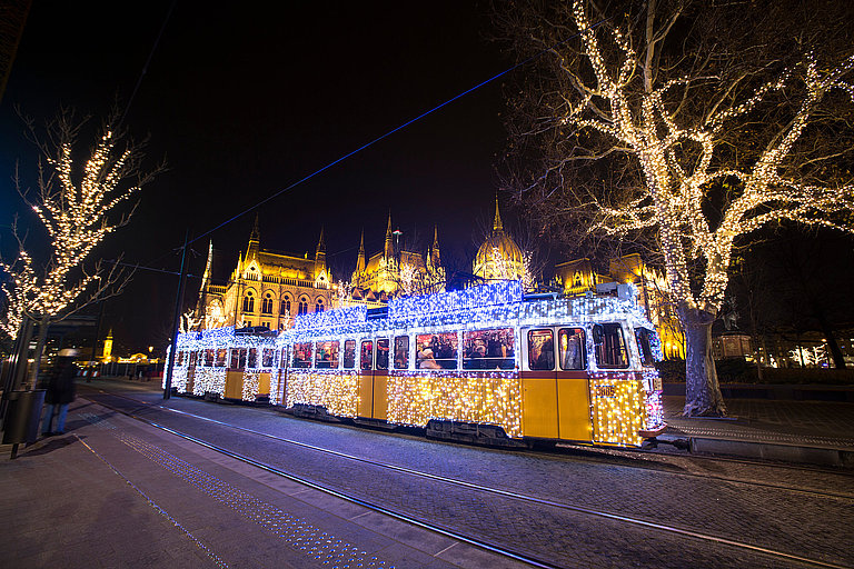 Festlich beleuchtete Weihnachtstram fährt nachts durch das winterliche Budapest.
