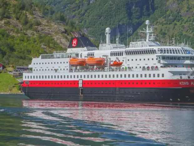 Kreuzfahrtschiff im Fjord vor steilen Bergen, blauem Wasser und grüner Landschaft.