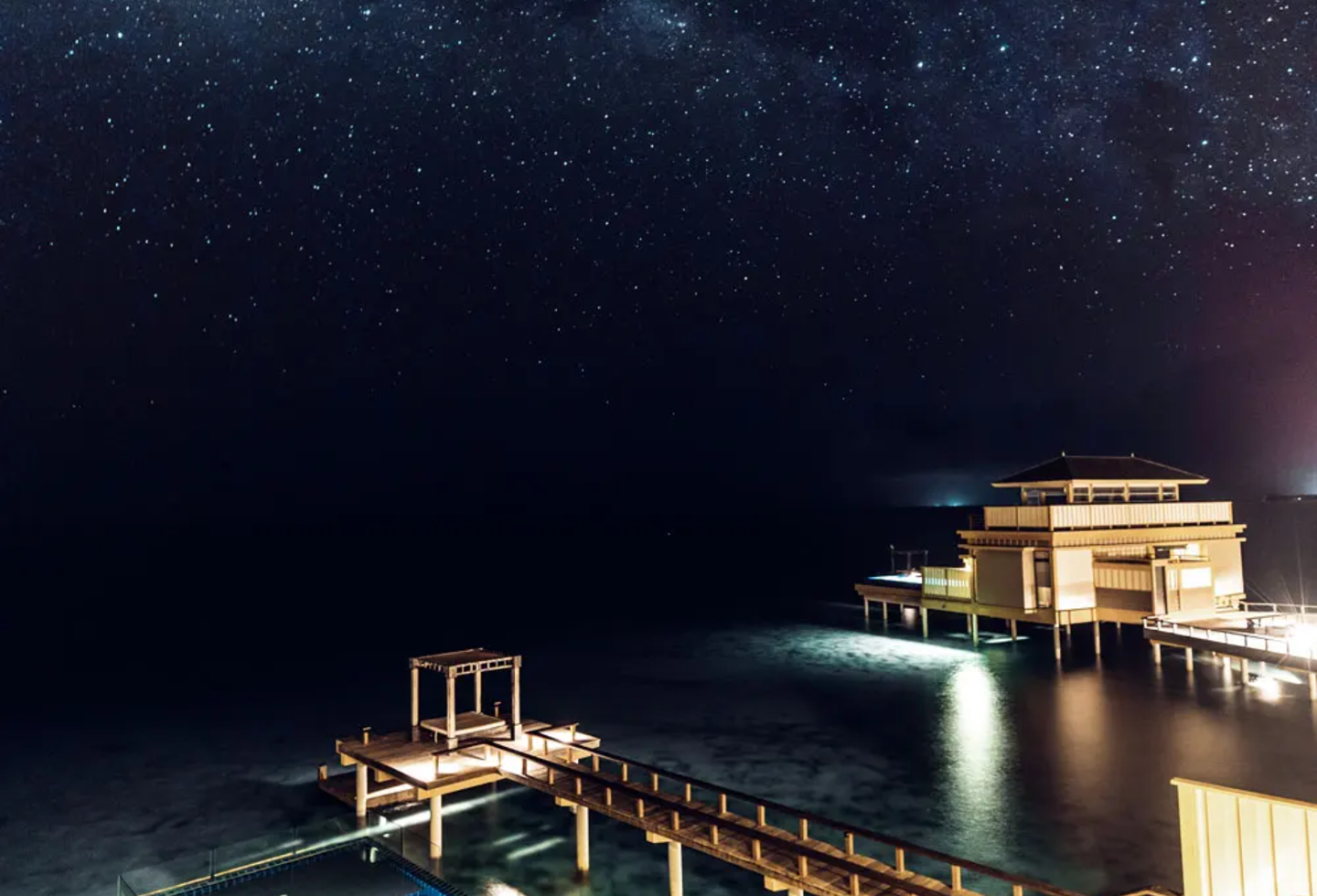 Beleuchteter Pool einer Wasservilla unter klarem Sternenhimmel in der Nacht.