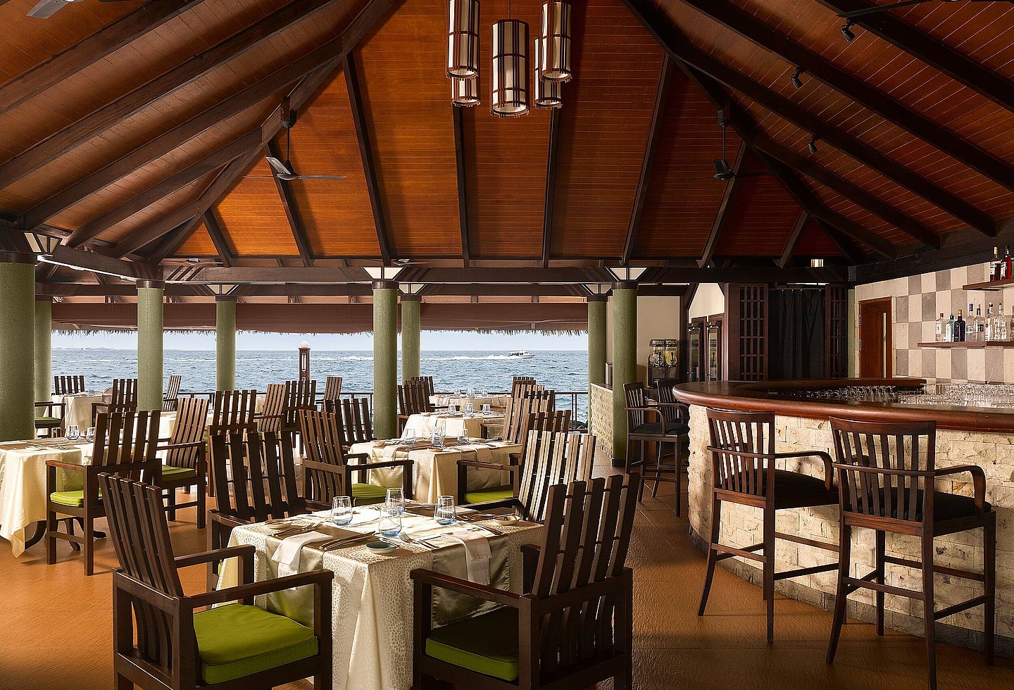 Restaurant mit Holzmöbeln, umgeben von tropischem Ambiente und Pflanzen.