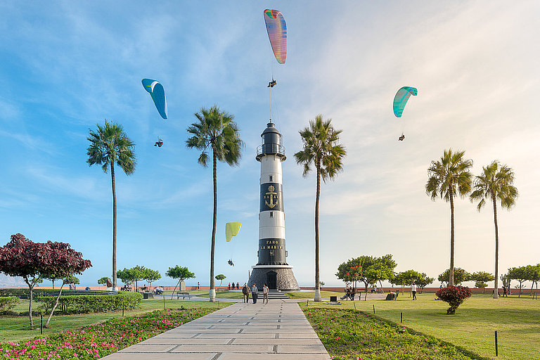 Leuchtturm mit Palmen, Blumenbeeten, Tandemspringern und Blick auf das Meer.