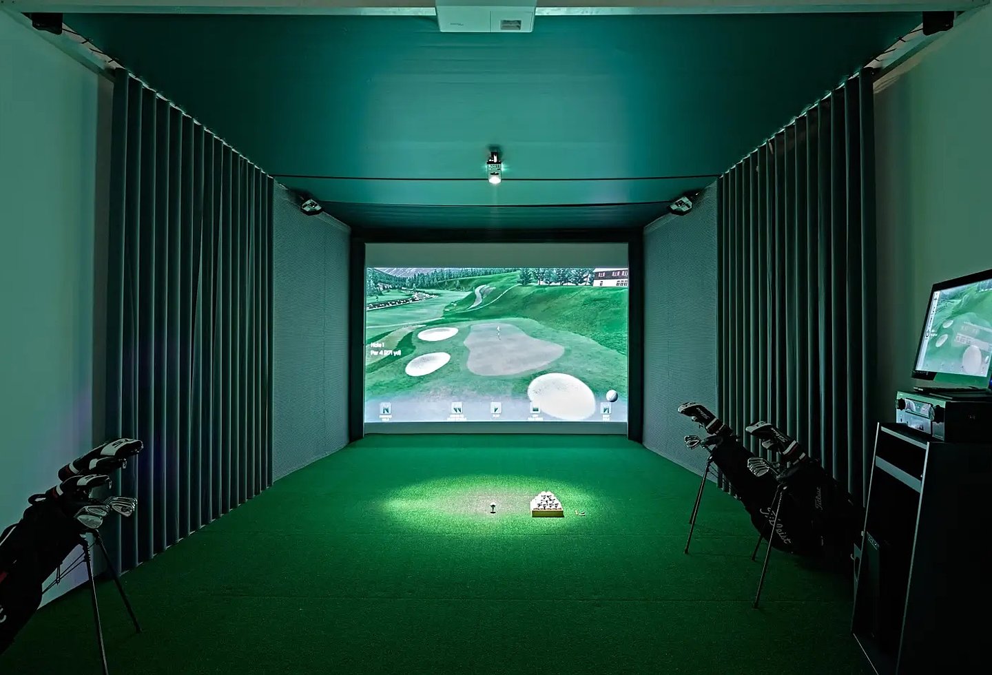 Indoor-Golfsimulator mit Abschlagmatte, Leinwand und virtueller Golfplatzansicht.