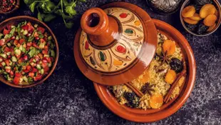Tajine mit traditionellem Gericht, umgeben von bunten Gewürzschalen.