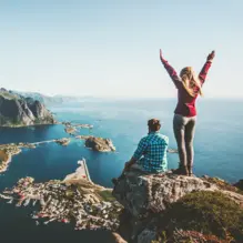 Wanderer auf Gipfel über Lofoten-Inseln, Fjorden und Bergen bei klarem Himmel.