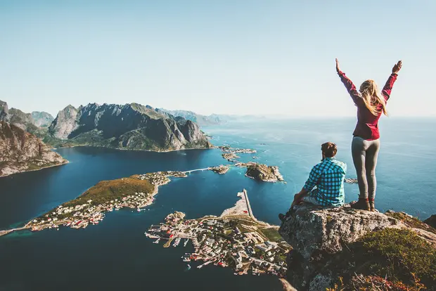 Wanderer auf Gipfel über Lofoten-Inseln, Fjorden und Bergen bei klarem Himmel.