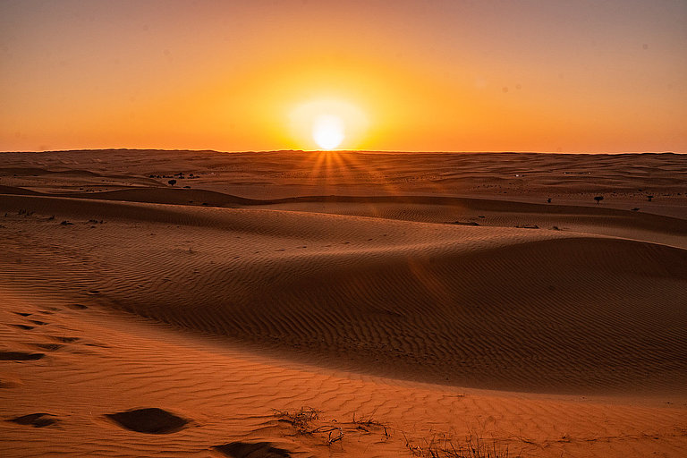 Sonnenuntergang über sanften Sanddünen in einer weiten, stillen Wüstenlandschaft.