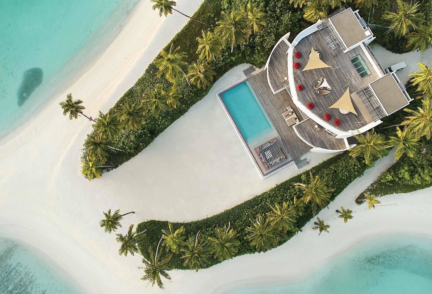 Luftaufnahme einer Strandvilla mit Pool, Palmen, weißem Sand und türkisblauem Meer.