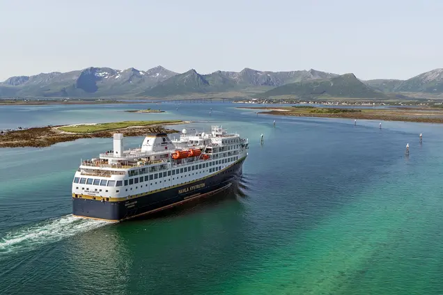 Ein malerisches Dorf mit bunten Häusern und Schiff liegt am Ufer eines ruhigen Fjords.