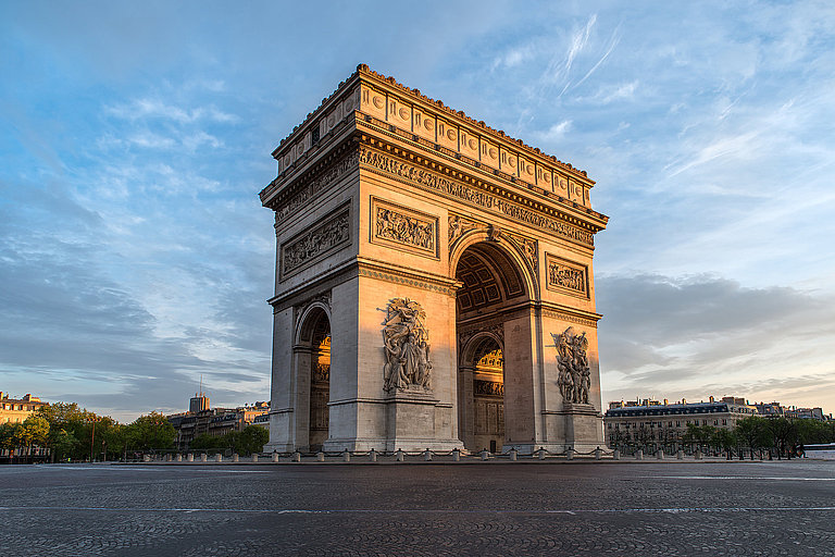 Arc de Triomphe im warmen Abendlicht unter blauem Himmel auf weiter Platzfläche.