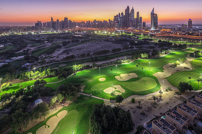 Beleuchteter Golfplatz im Vordergrund, dahinter die beleuchtete Skyline von Dubai.