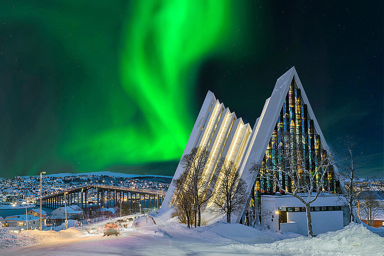Eismeerkathedrale in Tromsø mit grünem Nordlicht über verschneiter Winterlandschaft.