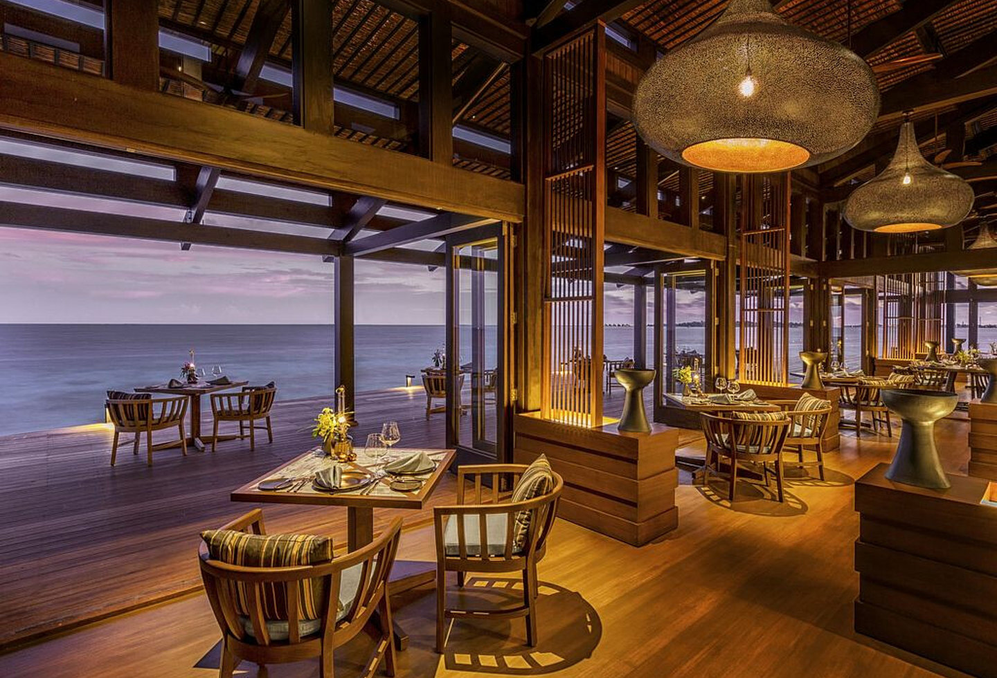 Restaurant bei Nacht, alles offen, Tische im Innen- und Außenbereich, große Lampenschirme an der Decke