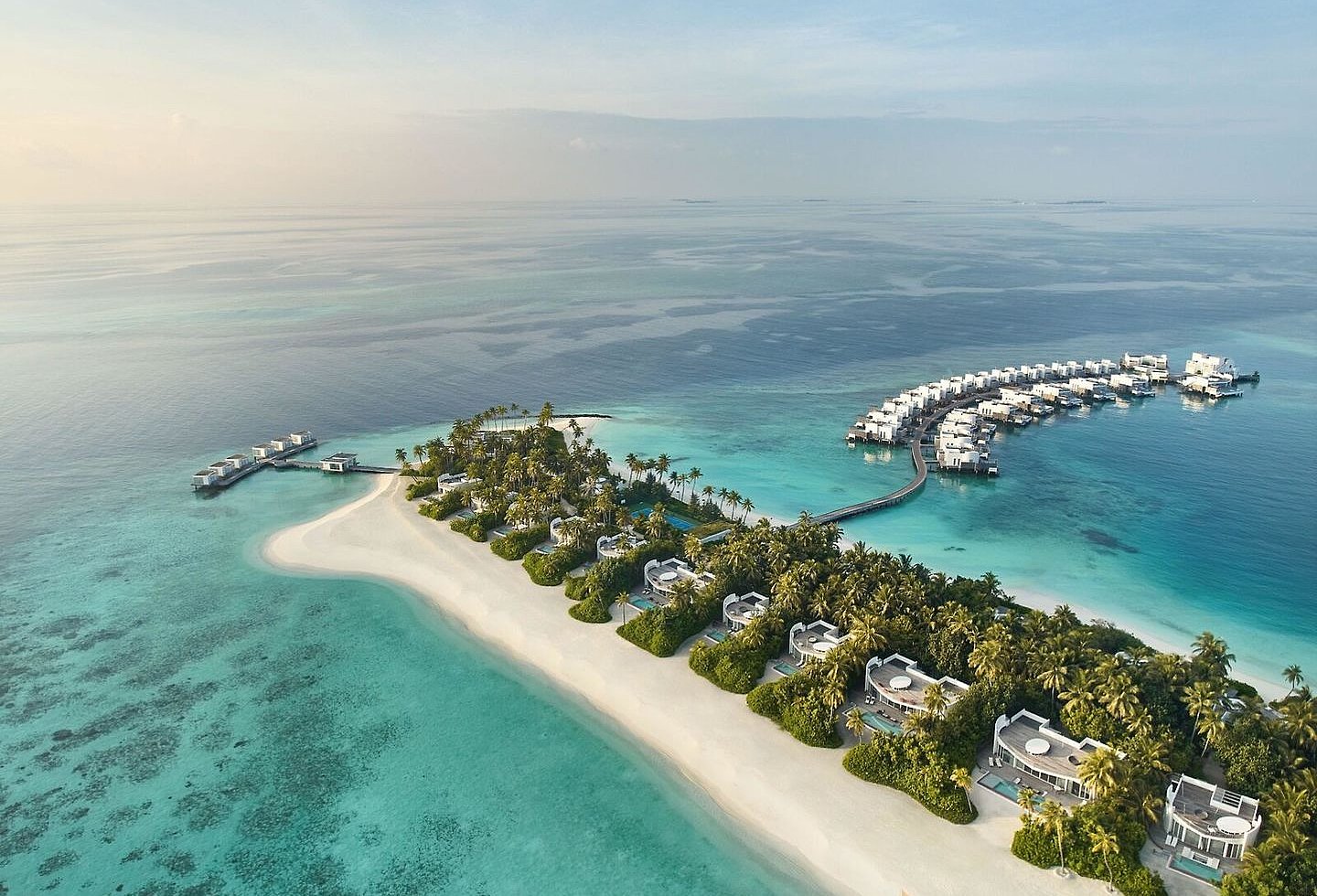 Luftaufnahme einer grünen Tropeninsel mit Sandstrand, Lagune und Wasservillen.