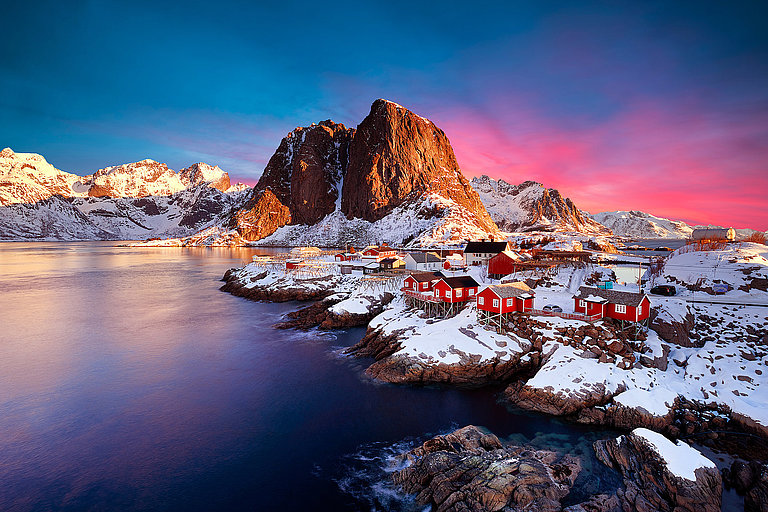 Verschneites Fischerdorf auf den Lofoten bei blau-rosafarbenem Abendlicht.