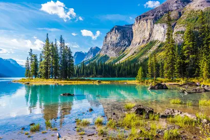 Türkisblauer Bergsee mit Felsen, Wald und hohen Gipfeln unter blauem Himmel.