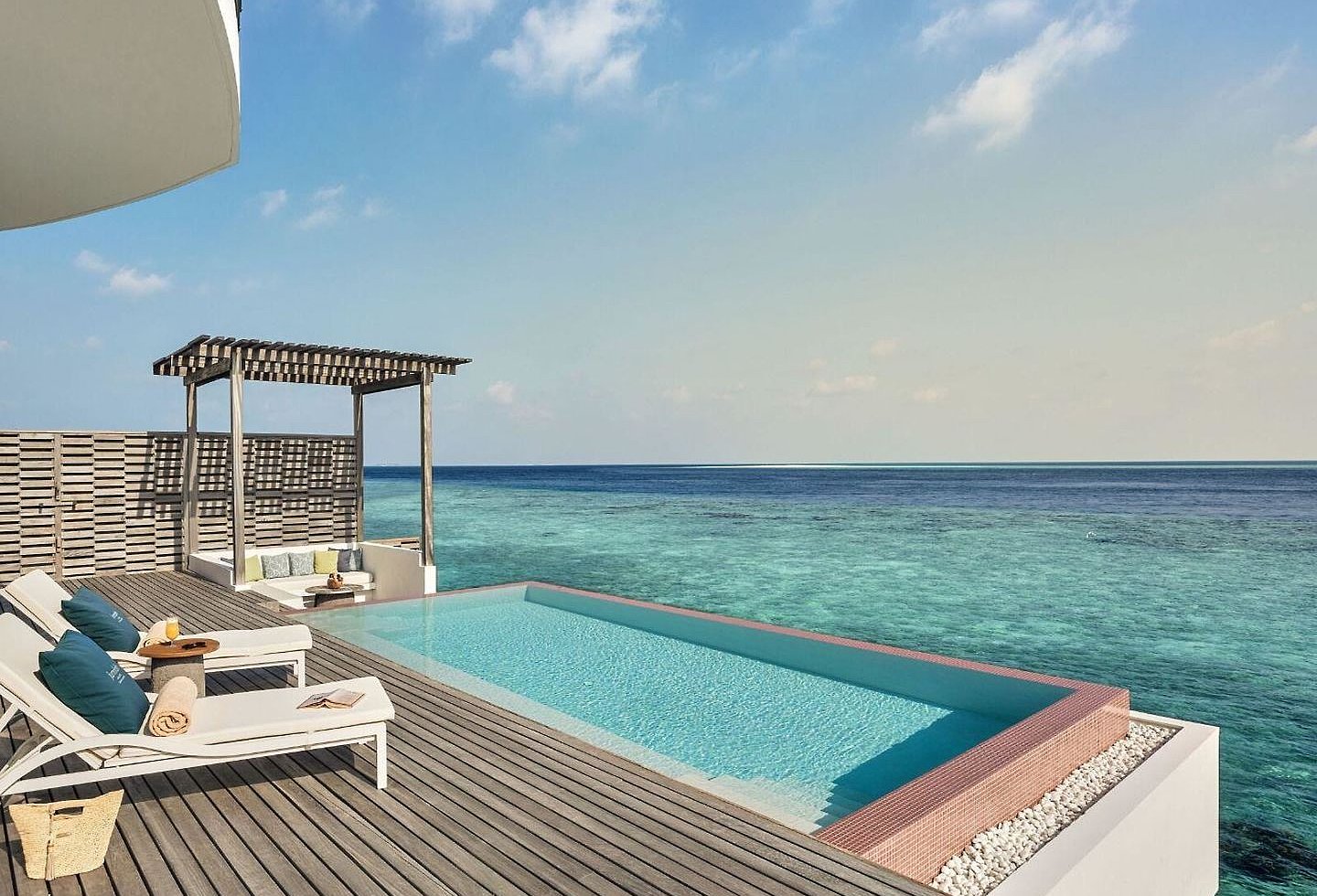 Infinitypool mit Sonnenliegen, Pergola und weitem Blick auf das blaue Meer.