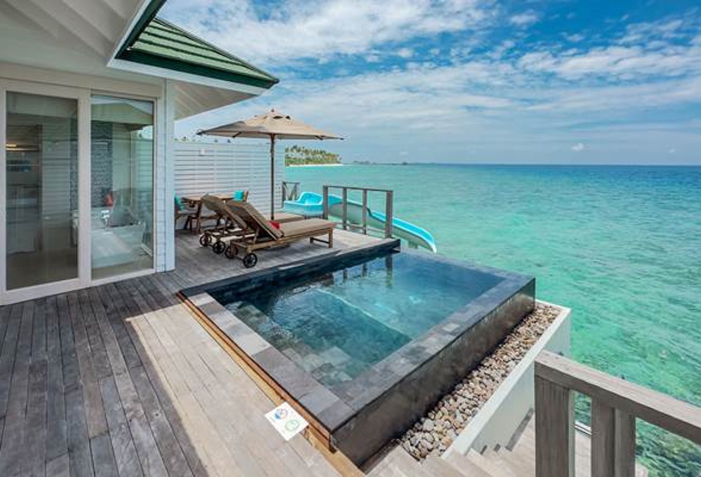Blick auf Terrasse einer Wasservilla mit Pool und Rutsche ins Meer, Liegen, Stiege ins Meer, Blick ins Badezimmer