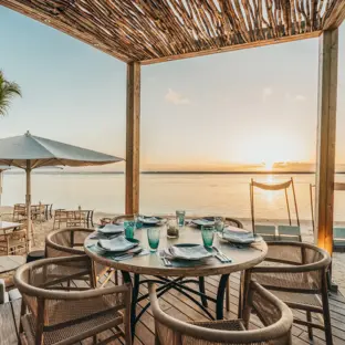 Strandrestaurant mit gedeckten Tischen, Strohdach und Blick auf Meer und SOnnenuntergang.