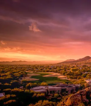 Golfplatz und Häuser bei Sonnenuntergang vor felsigen Bergen in Scottsdale.