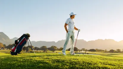Golfer schlägt auf grünem Fairway vor weitem Platz, Hügeln und hellem Himmel.