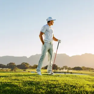 Golfer schlägt auf grünem Fairway vor weitem Platz, Hügeln und hellem Himmel.