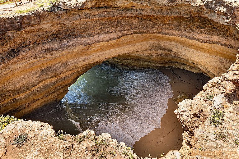 Benagil-Meeresgrotte an der Algarve mit Felsbogen, Sandstrand und blauem Meer.