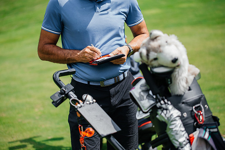 Golfer mit Golftasche und Schlägern auf grünem Rasen während einer Runde Golf.