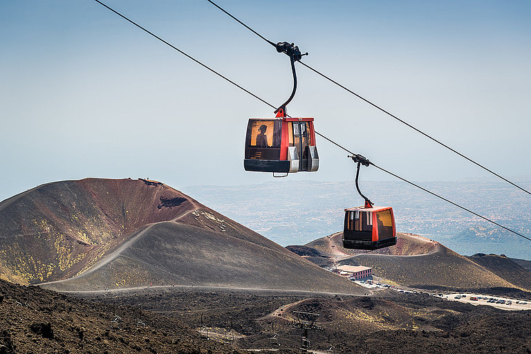 Zwei Abteile der Ätna Seilbahn hängen über karger Landschaft in Sizilien.