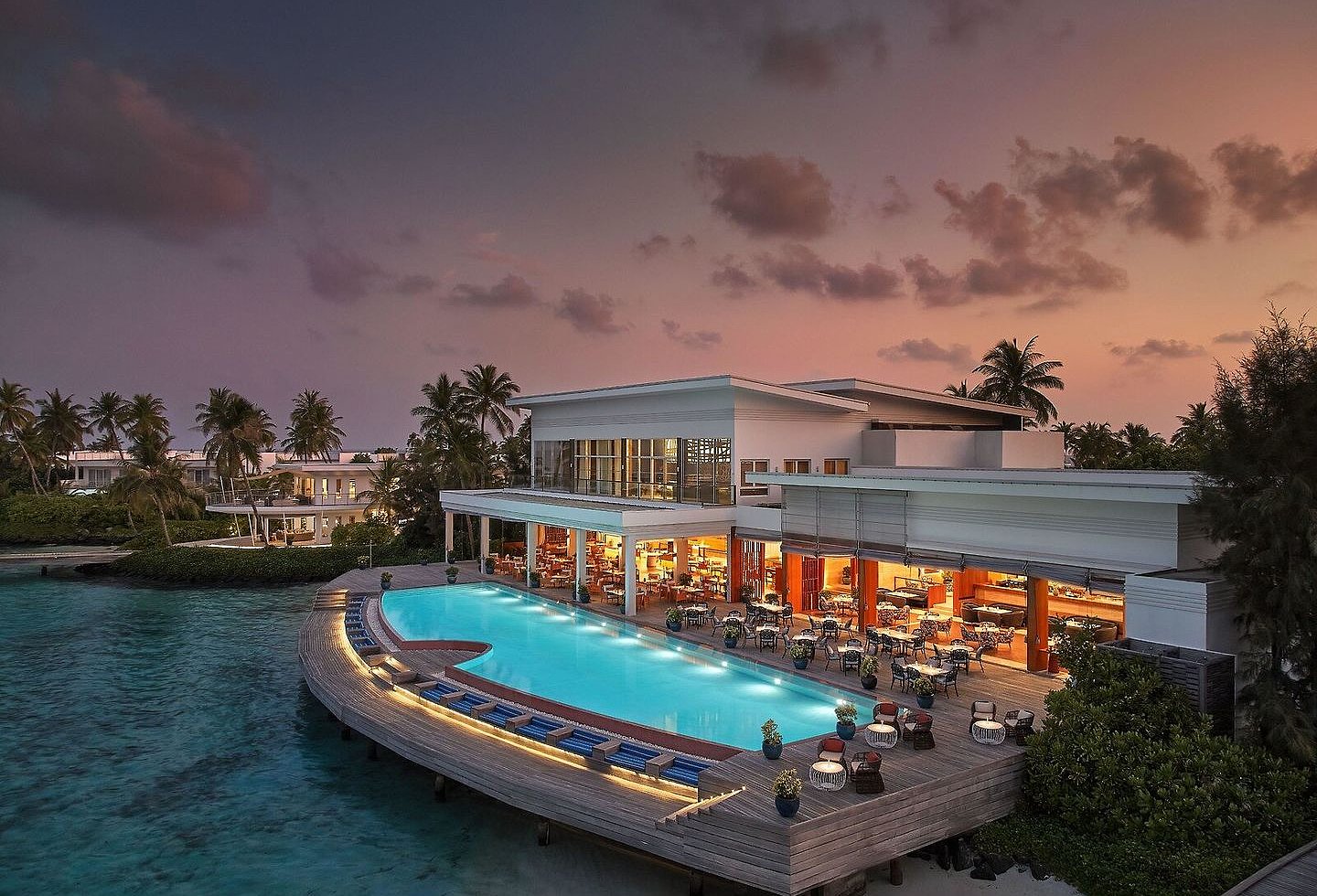 Beleuchteter Infinitypool eines tropischen Inselresorts am Meer bei Sonnenuntergang.