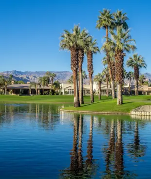 Golfplatz mit Palmen, Wasserfläche und Bergkulisse unter einem tiefblauen Himmel.