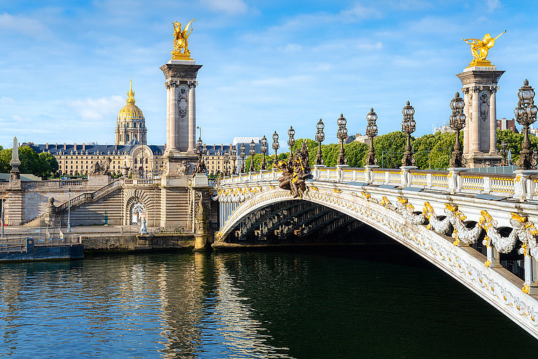 Prunkvolle Brücke über die Seine mit goldenen Figuren unter hellem Himmel in Paris.