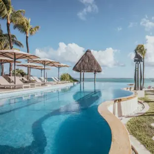Poollandschaft mit Palmen, Meerblick und Strohdachpavillion im tropischen Resort.