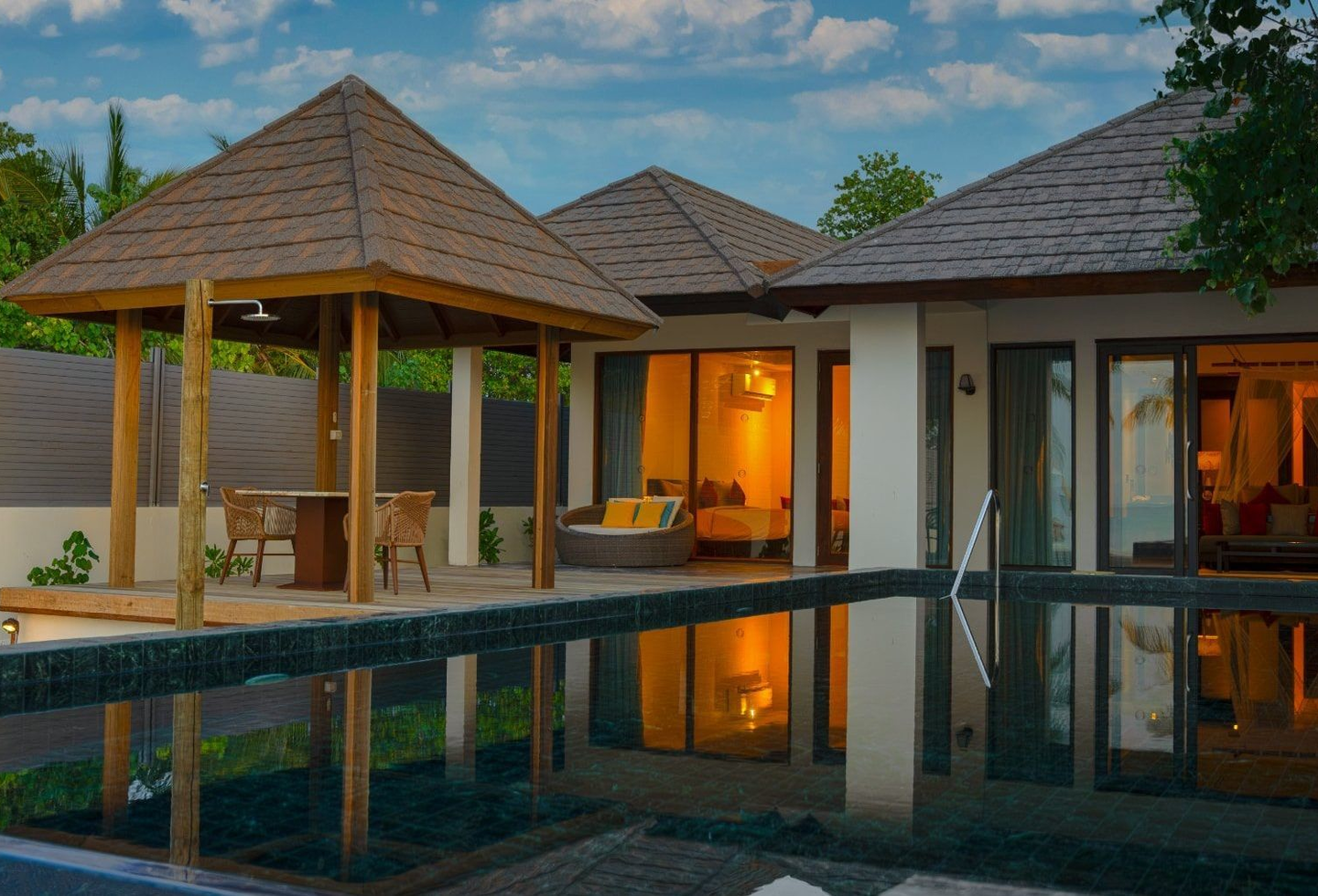 Blick vom privaten Pool über die Terrasse in 2 beleuchtete Räume einer Villa.