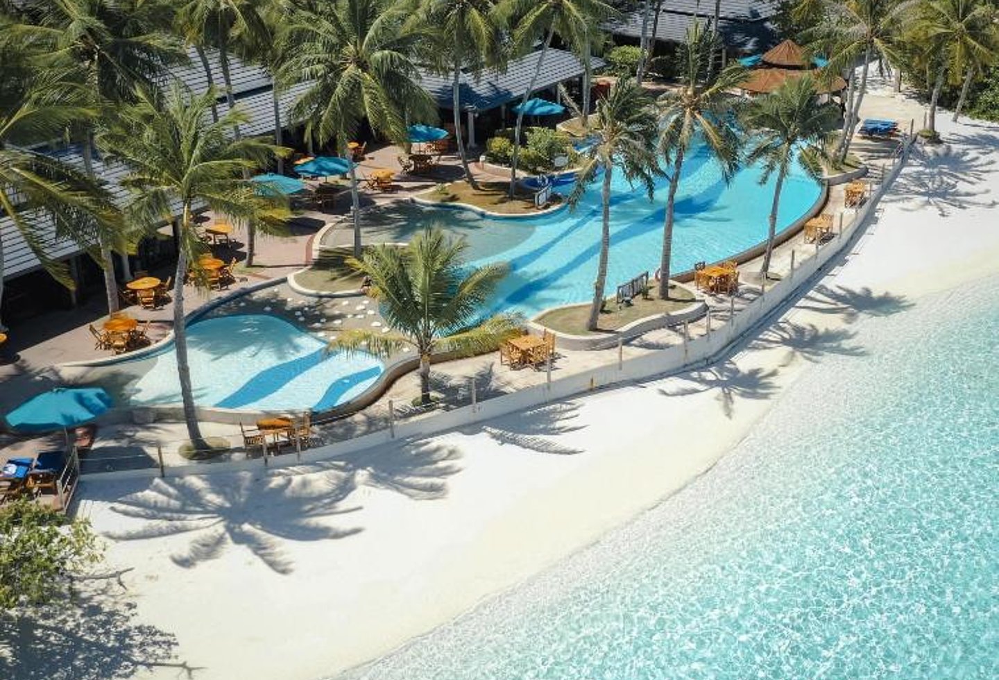 Luftaufnahme eines tropischen Strandresorts mit Pool, Palmen und türkisblauem Meer.