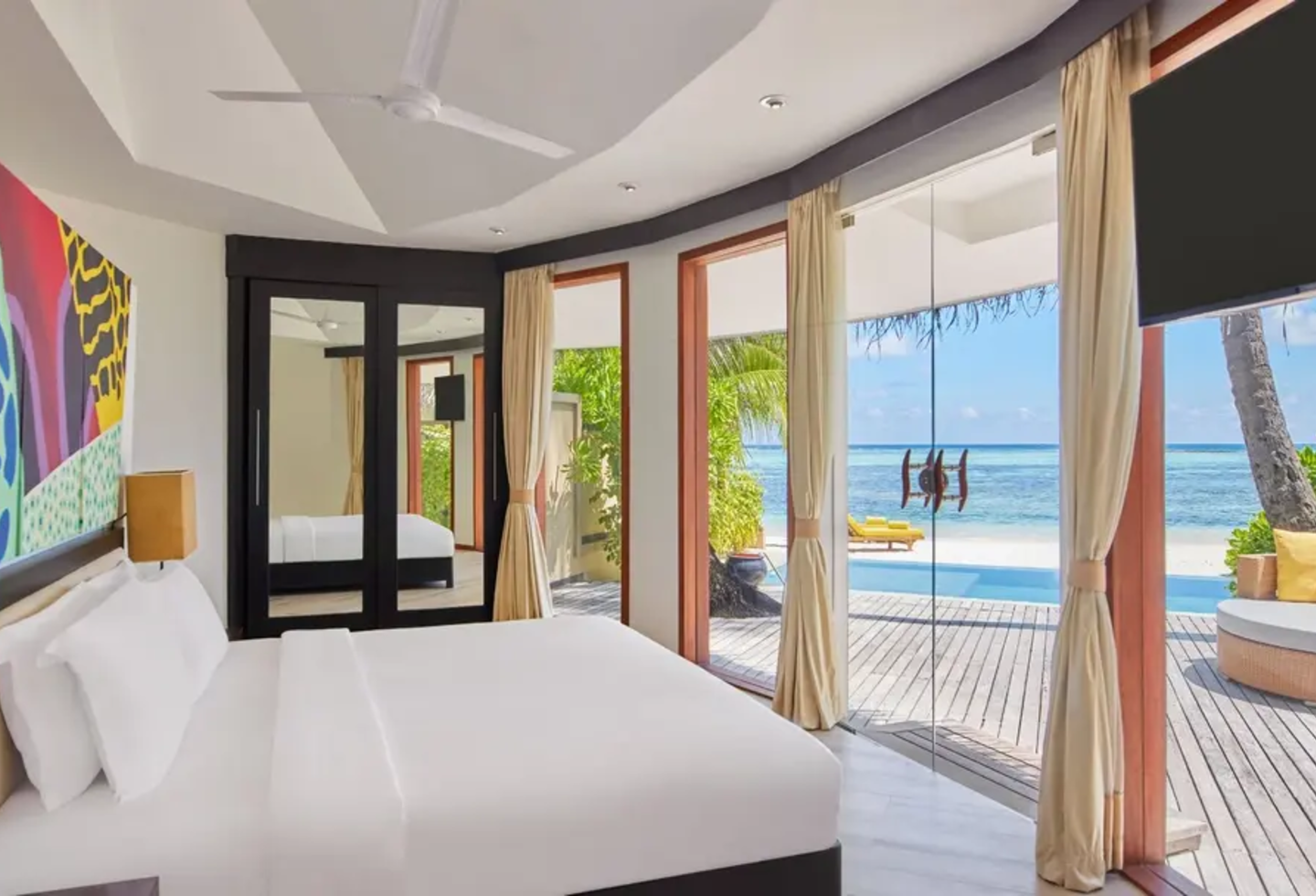 Bett, dahinter buntes Gemälde, davor Terrasse mit Pool, Meer im Anschluss.